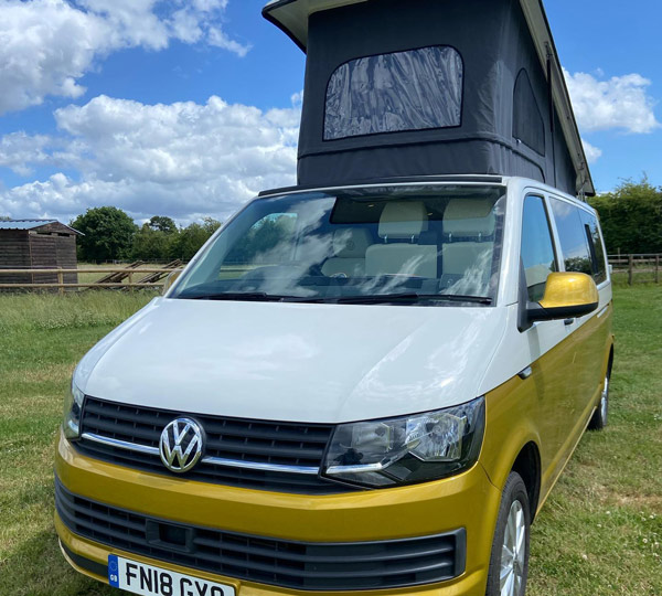 Volkswagen camper van with a roof tent parked in a grassy field under a blue sky providing an ideal outdoor adventure experience